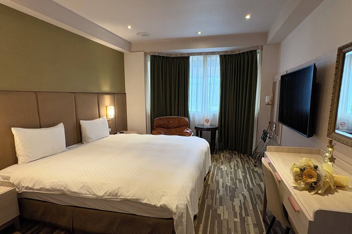 A hotel room with a large bed, a desk, a chair, a television, and a window with curtains.