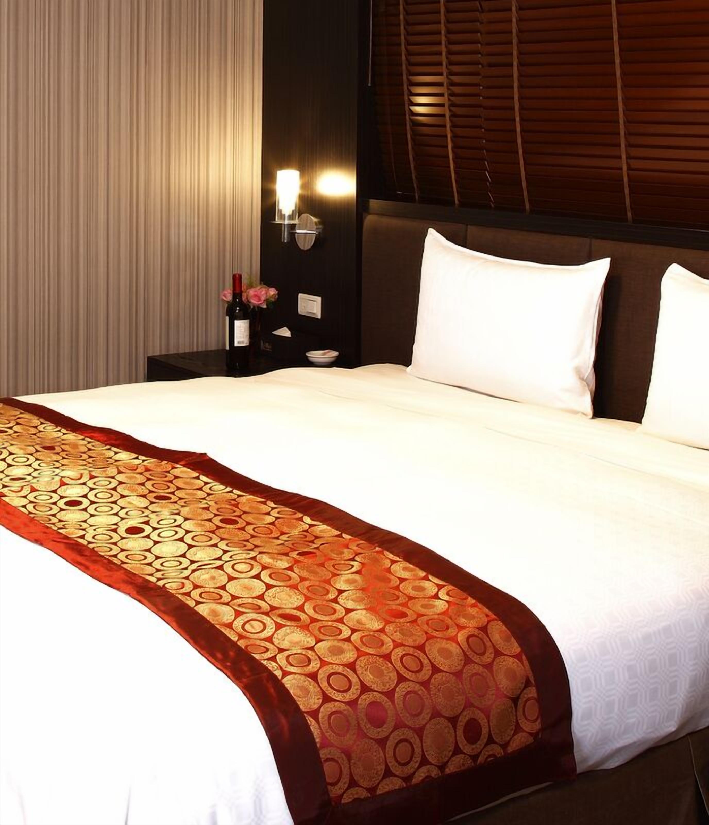 Une chambre d’hôtel avec un grand lit, une table de chevet avec une lampe et une fenêtre avec des stores.