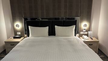 A hotel room with a large bed, two bedside tables, a nightstand, a wall-mounted phone, and a mirror with lights.