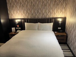 Una habitación de hotel con una cama grande, dos mesitas de noche, una lámpara de pared y un reloj de pared.