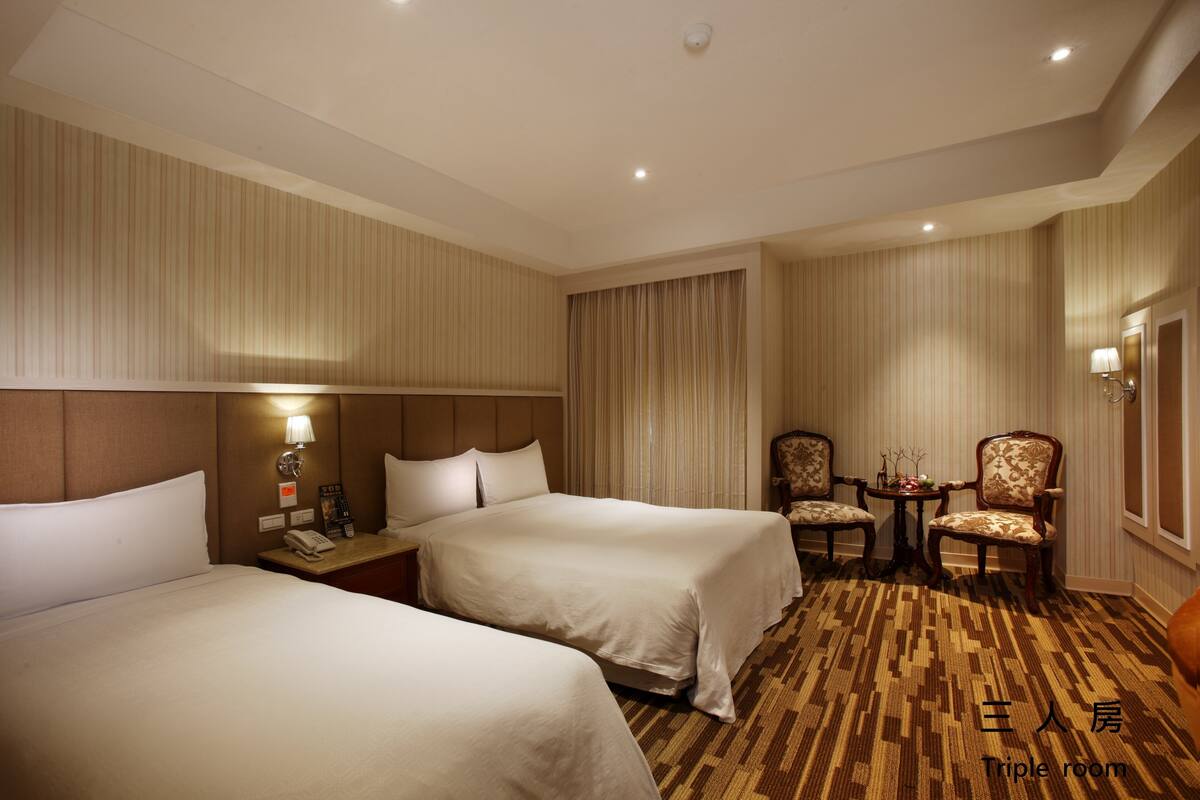A triple room with two beds, a small table with a lamp, and a chair.