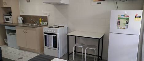 A compact kitchen with a stove, microwave, and sink. There is a small table with two stools and a refrigerator with a sticker.