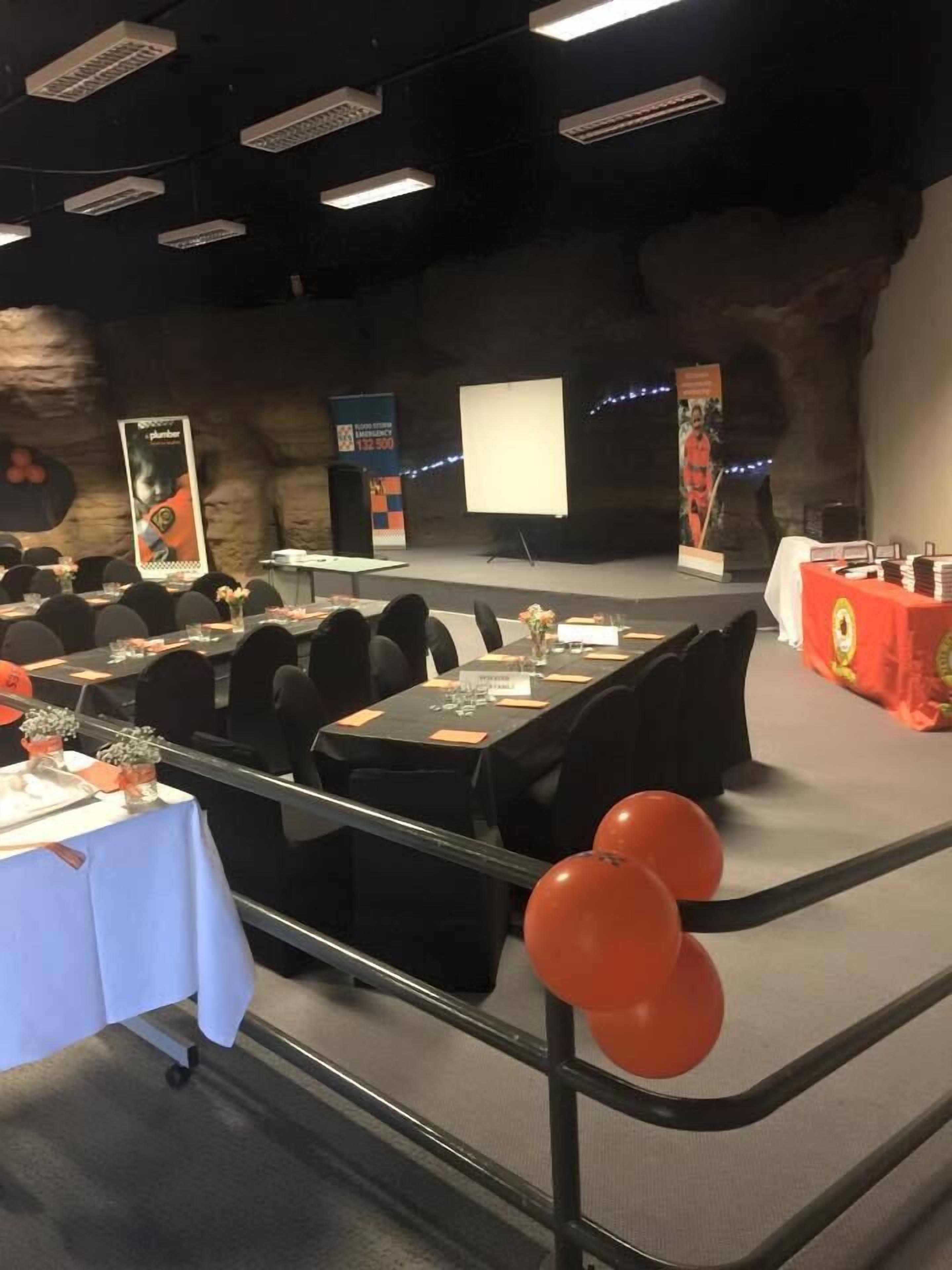 A conference room with tables, chairs, a stage, banners, and a projector screen.