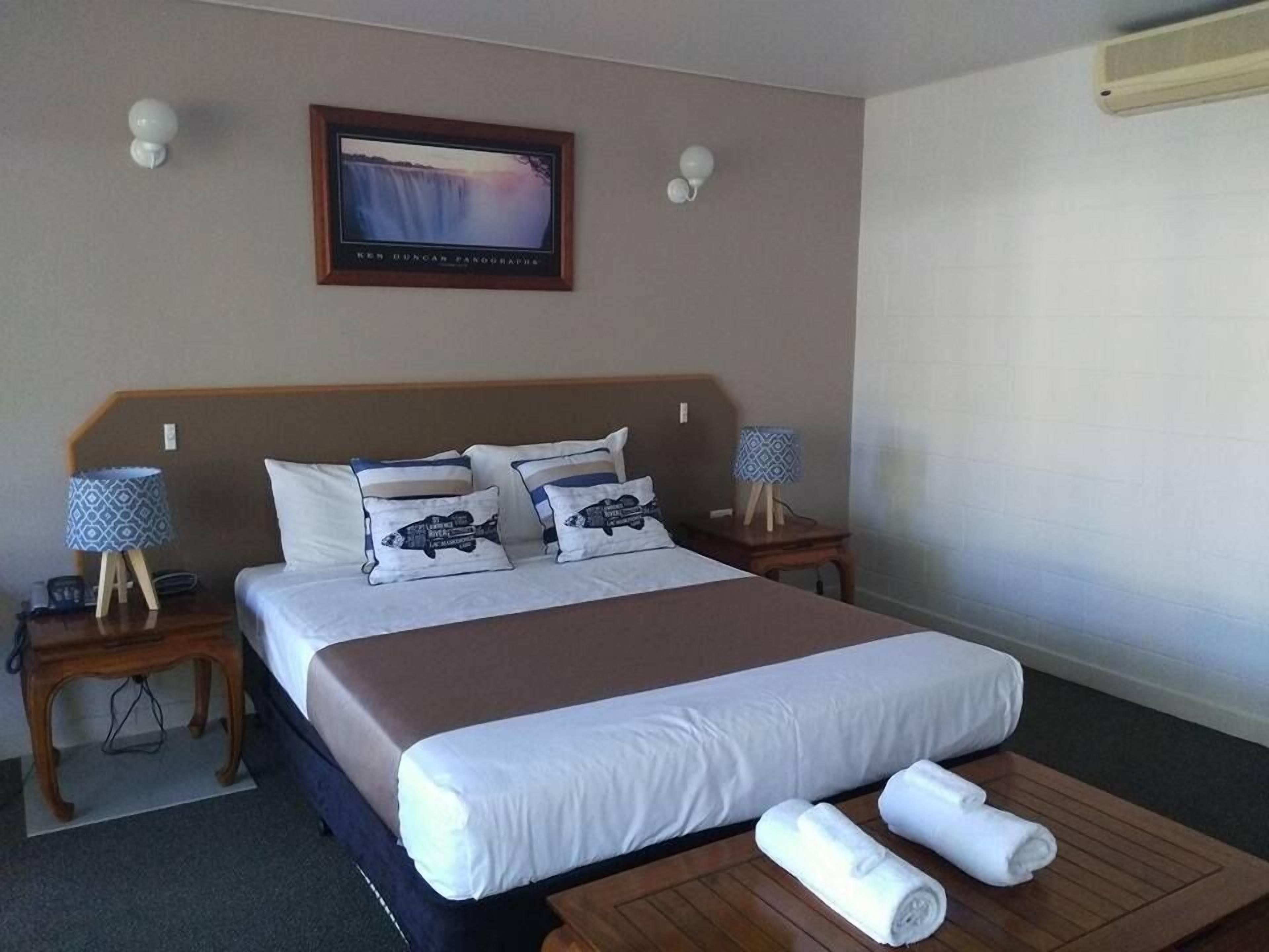 Habitación de hotel con una cama grande, dos mesitas de noche, un cuadro en la pared y una mesa de centro de madera con toallas.