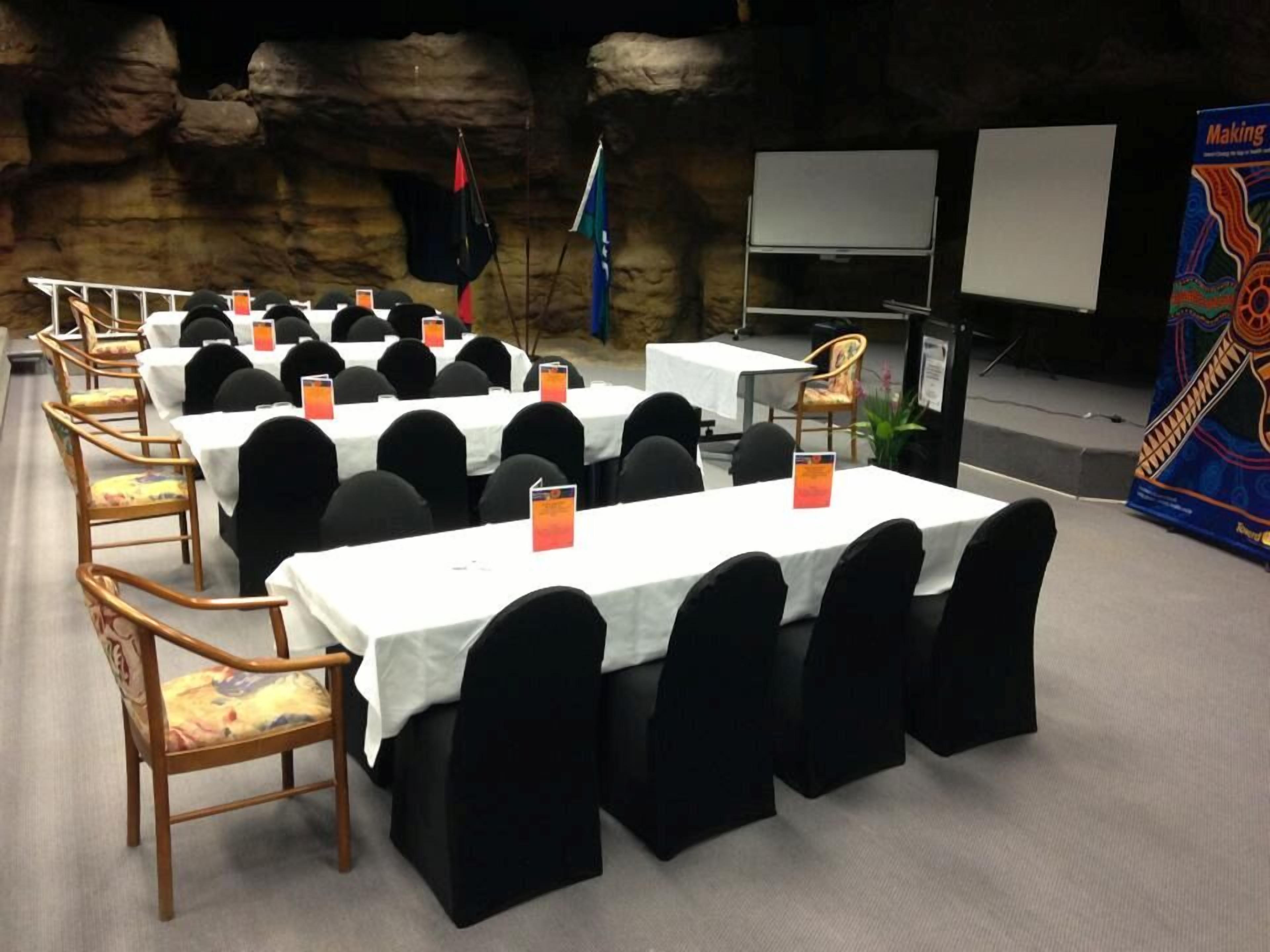 Un salón de conferencias con mesas y sillas, un escenario con una pizarra y una bandera.