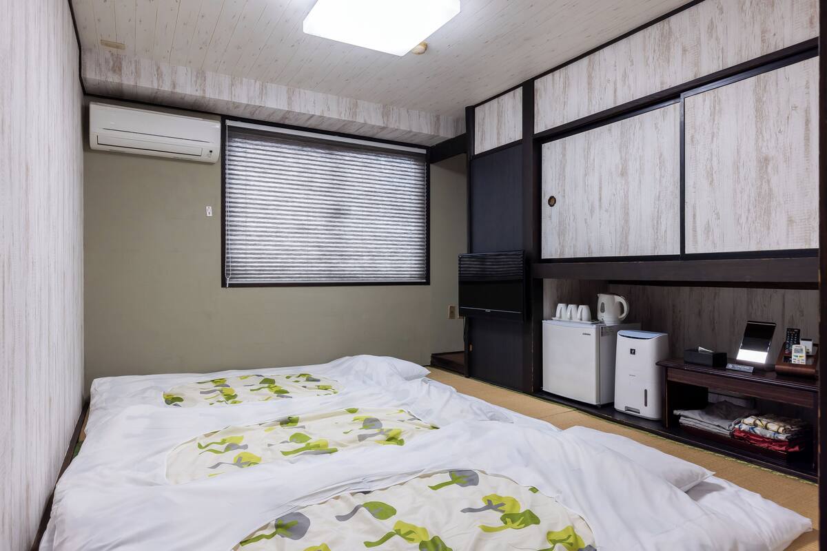 A hotel room with two beds, a minibar, a desk, and a window with blinds.