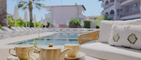 A poolside area with lounge chairs, a table with a teapot and cups, and a building in the background.