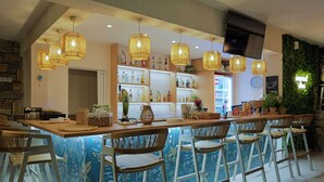 Zona de bar con sillas de mimbre, una barra con botellas y un televisor montado en la pared.