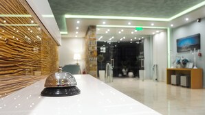Zona de recepción de un hotel con pared de madera texturizada, un mostrador de recepción con cúpula de vidrio e iluminación verde en el techo moderno.