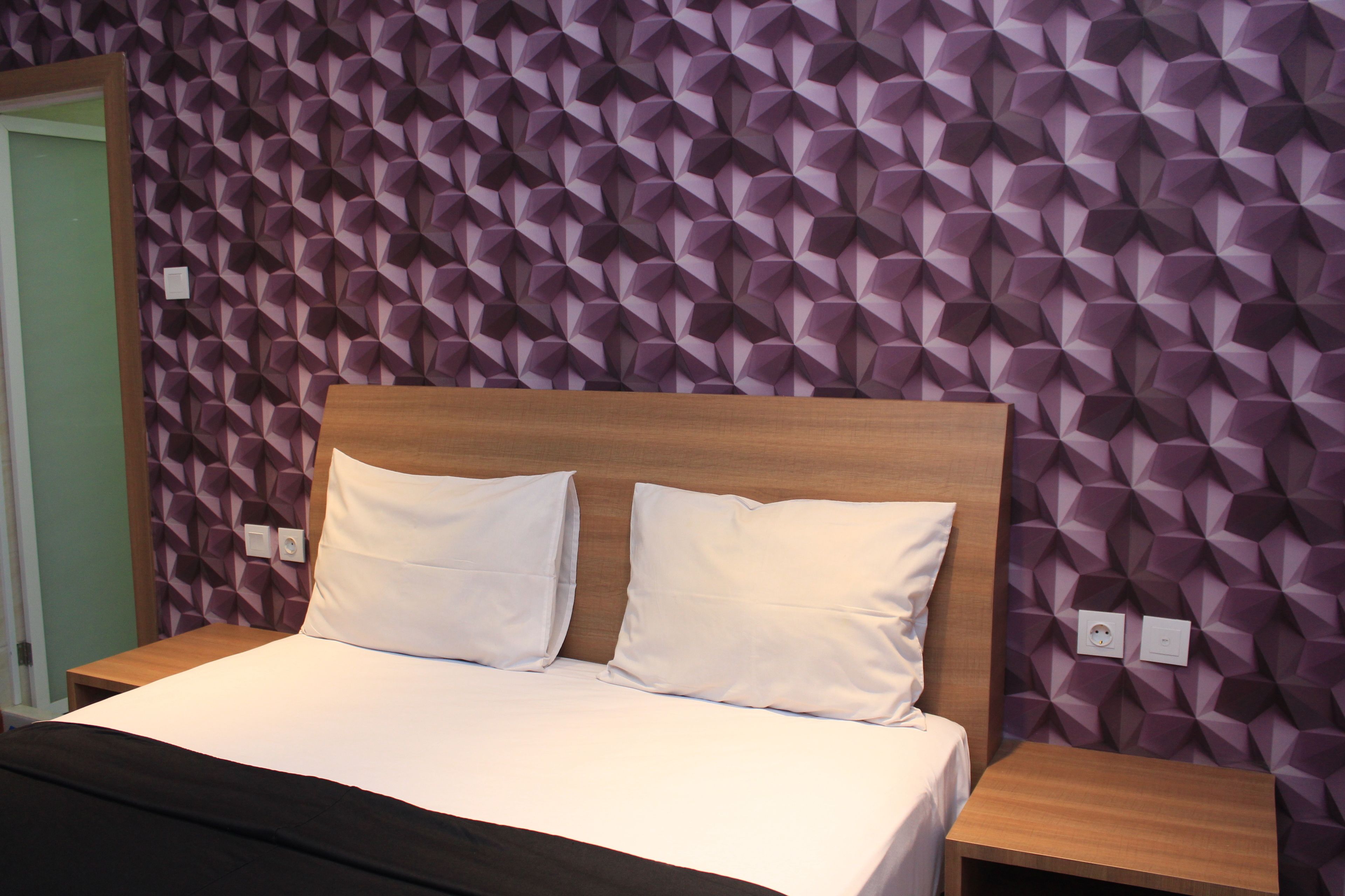 A bed with white bedding and two pillows, a wooden headboard, and a nightstand with a lamp.