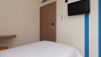Un dormitorio con una cama, un televisor montado en la pared, una puerta y un enchufe.