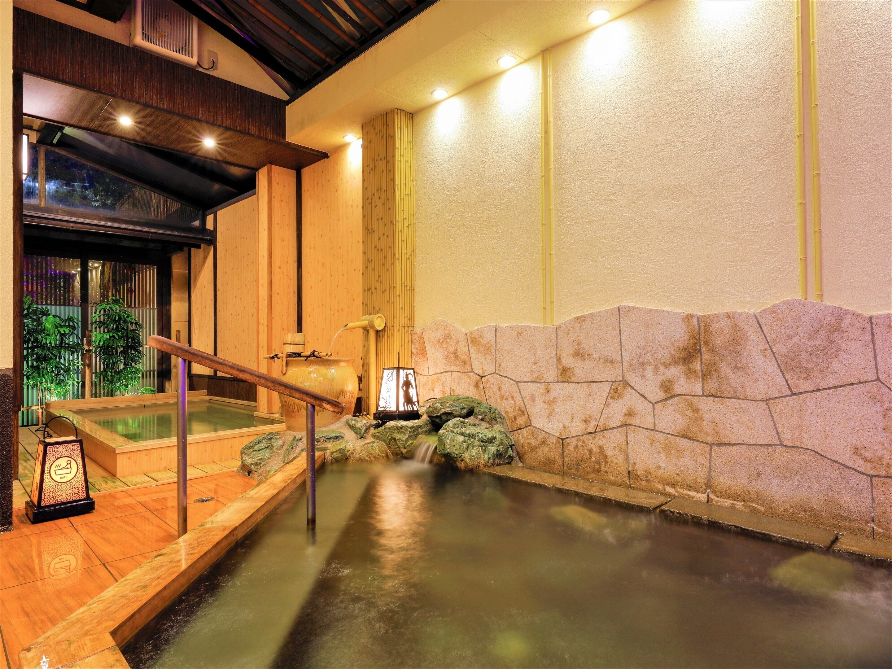 A traditional Japanese onsen with a wooden bath, a stone wall, and a bamboo water spout.