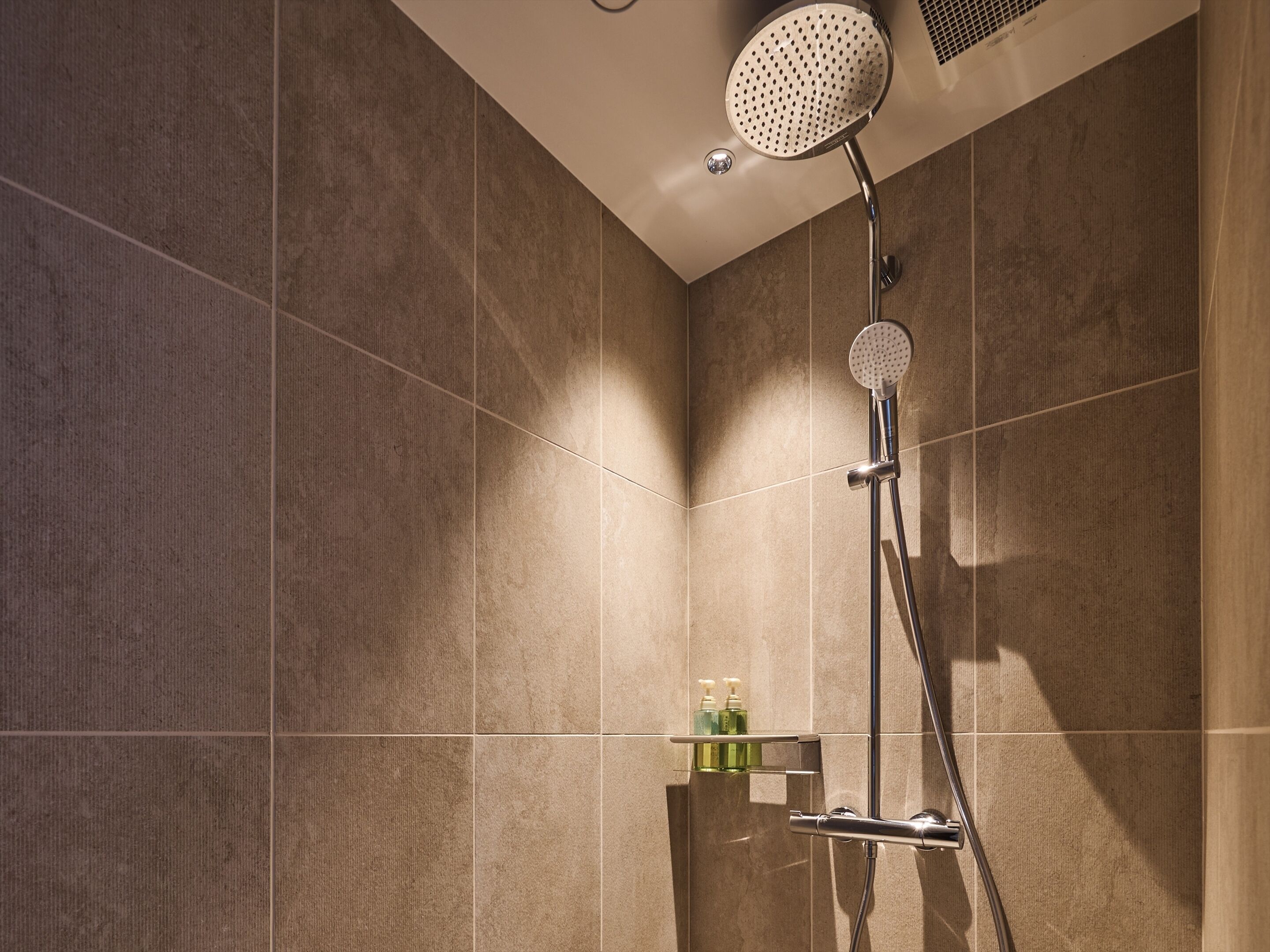 A modern shower with a handheld showerhead and a wall-mounted control.