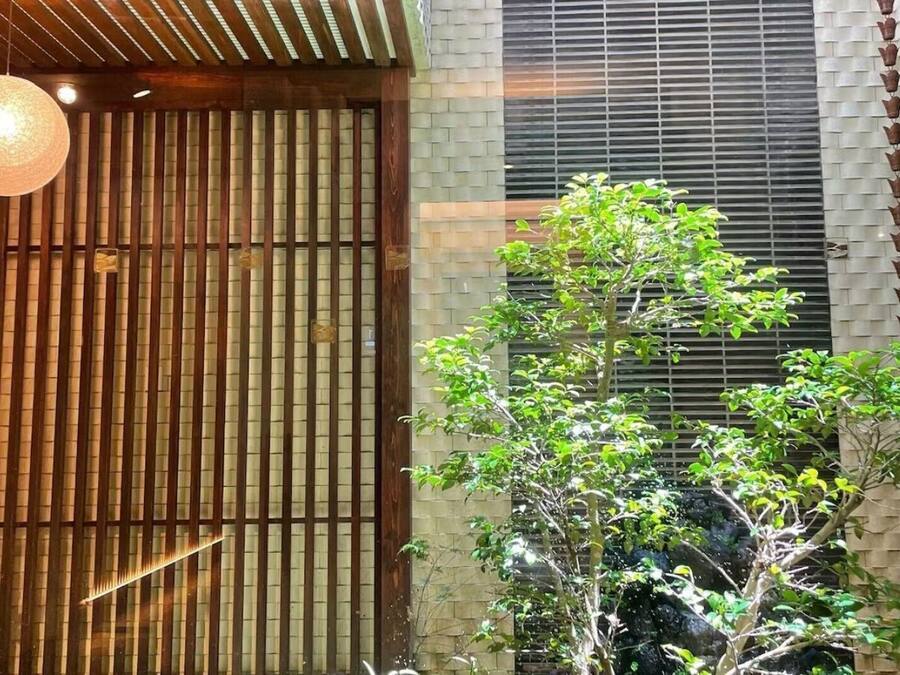 A building with a wooden slat entrance, a brick wall, and a small tree in front.