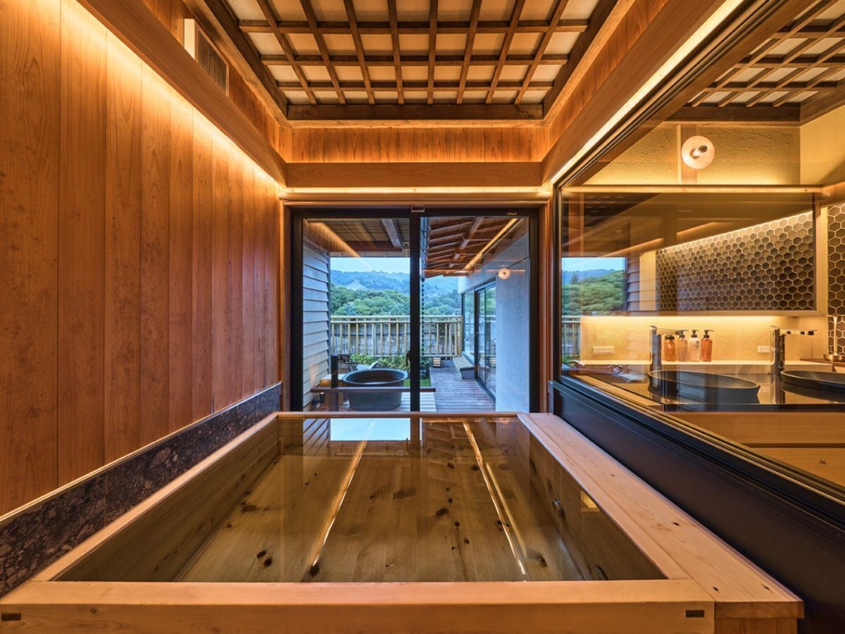 Un ba ño moderno con suelo de madera, cabina de vidrio y vistas a un paisaje montañoso.