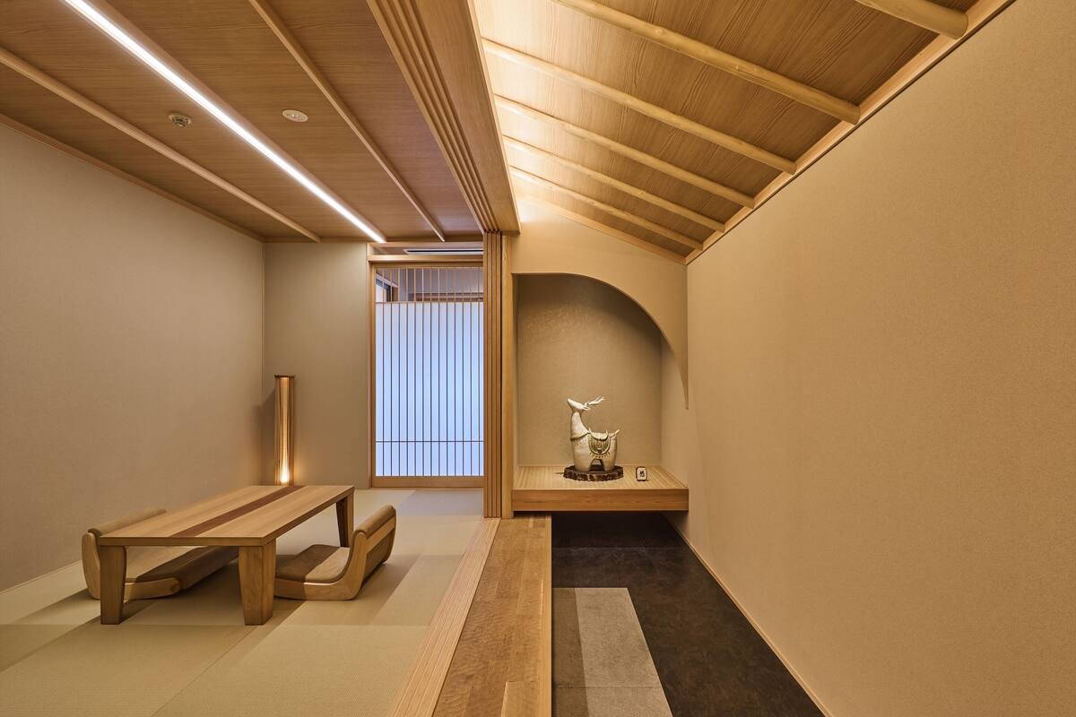 A traditional Japanese room with tatami flooring, a low wooden table, a bench, a decorative sculpture, and a sliding door leading to a balcony.