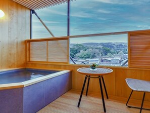 A modern bathroom with a wooden bathtub, a small round table with a vase, and a chair. - Hotel New Wakasa (Nara)