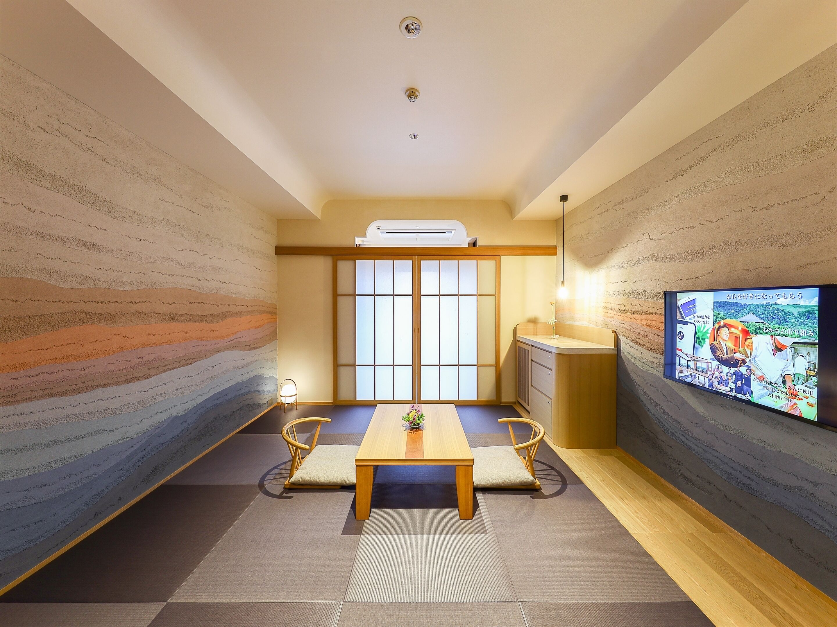 Um quarto tradicional japonês com tatames, uma mesa de madeira baixa e uma televisão fixada na parede.