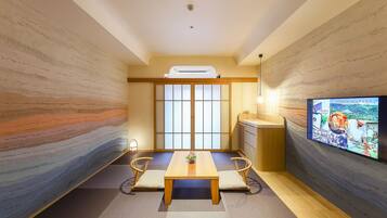 Um quarto tradicional japonês com tatames, uma mesa de madeira baixa e uma televisão fixada na parede.