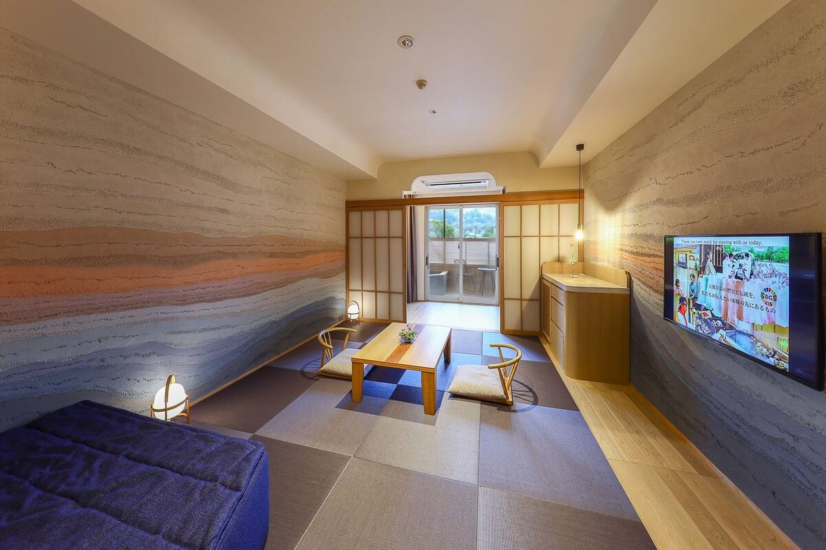 A modern living room with tatami flooring, a low table, chairs, a sofa, and a TV mounted on the wall.