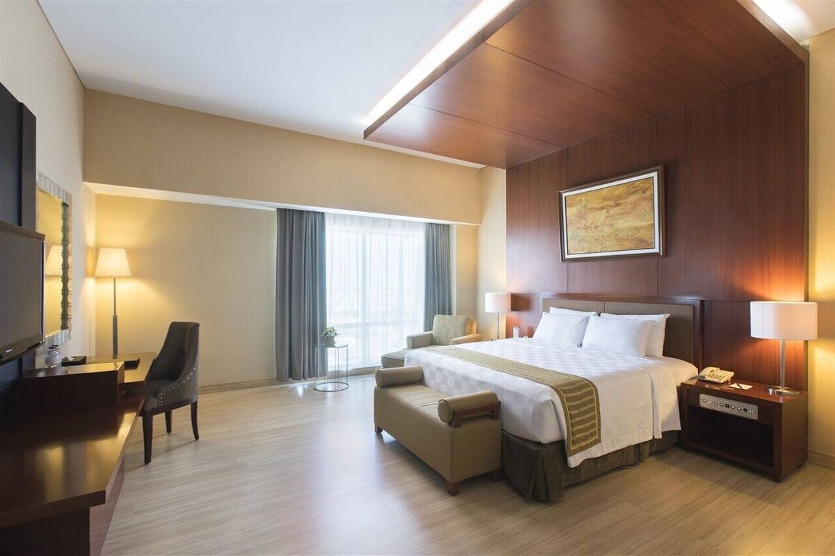 A hotel room with a large bed, a desk, a chair, a bedside table, and a television.