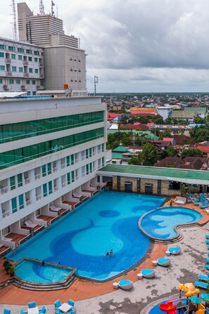 A hotel with a large swimming pool, multiple balconies, and a view of the surrounding cityscape. - Claro Makassar (Makassar)
