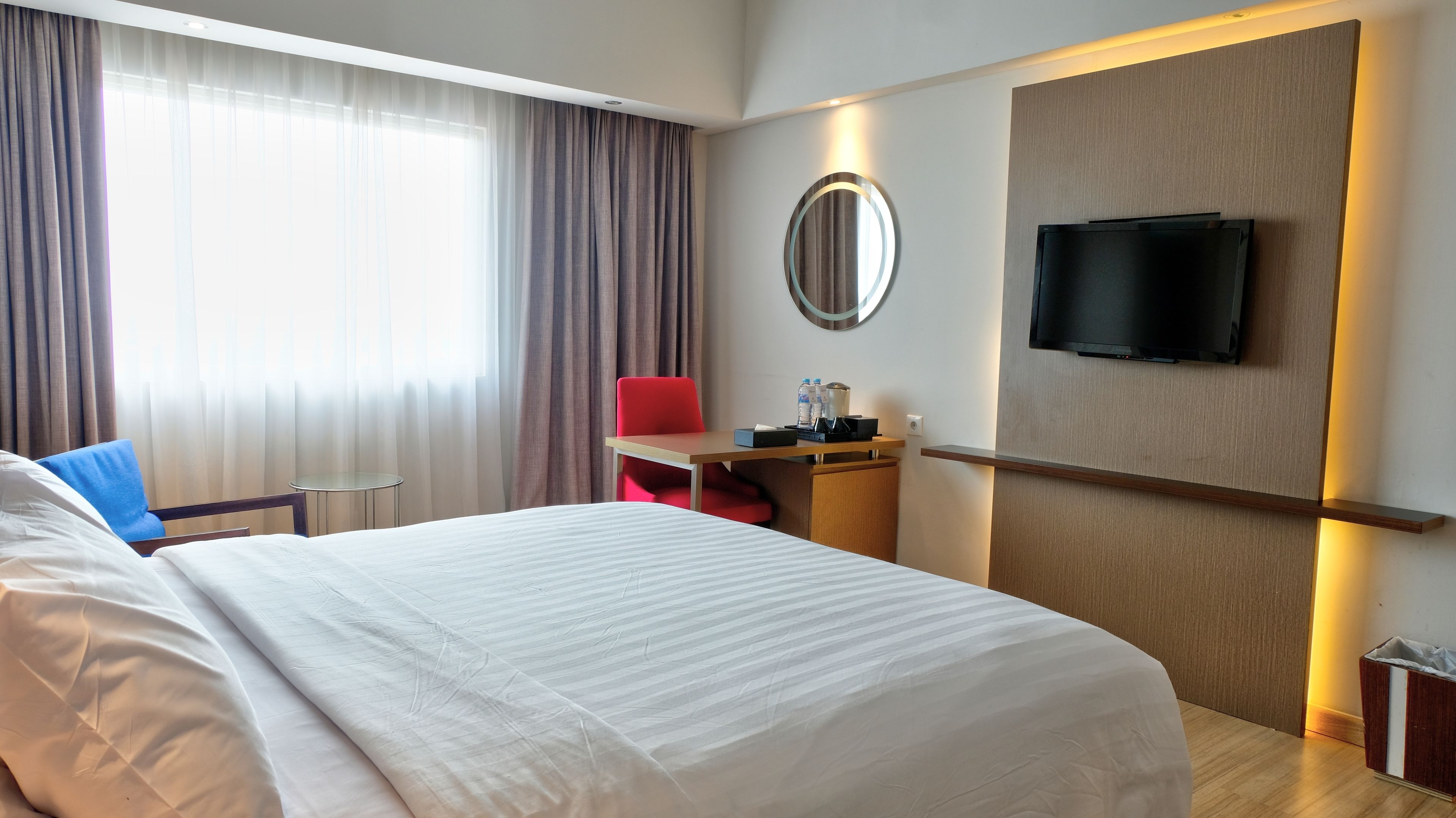 Habitación de hotel con una cama grande, un escritorio con silla, televisión montada en la pared y ventana con cortinas.