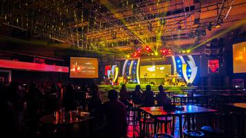 A concert venue with a stage, audience seating, and a large screen displaying a performer.