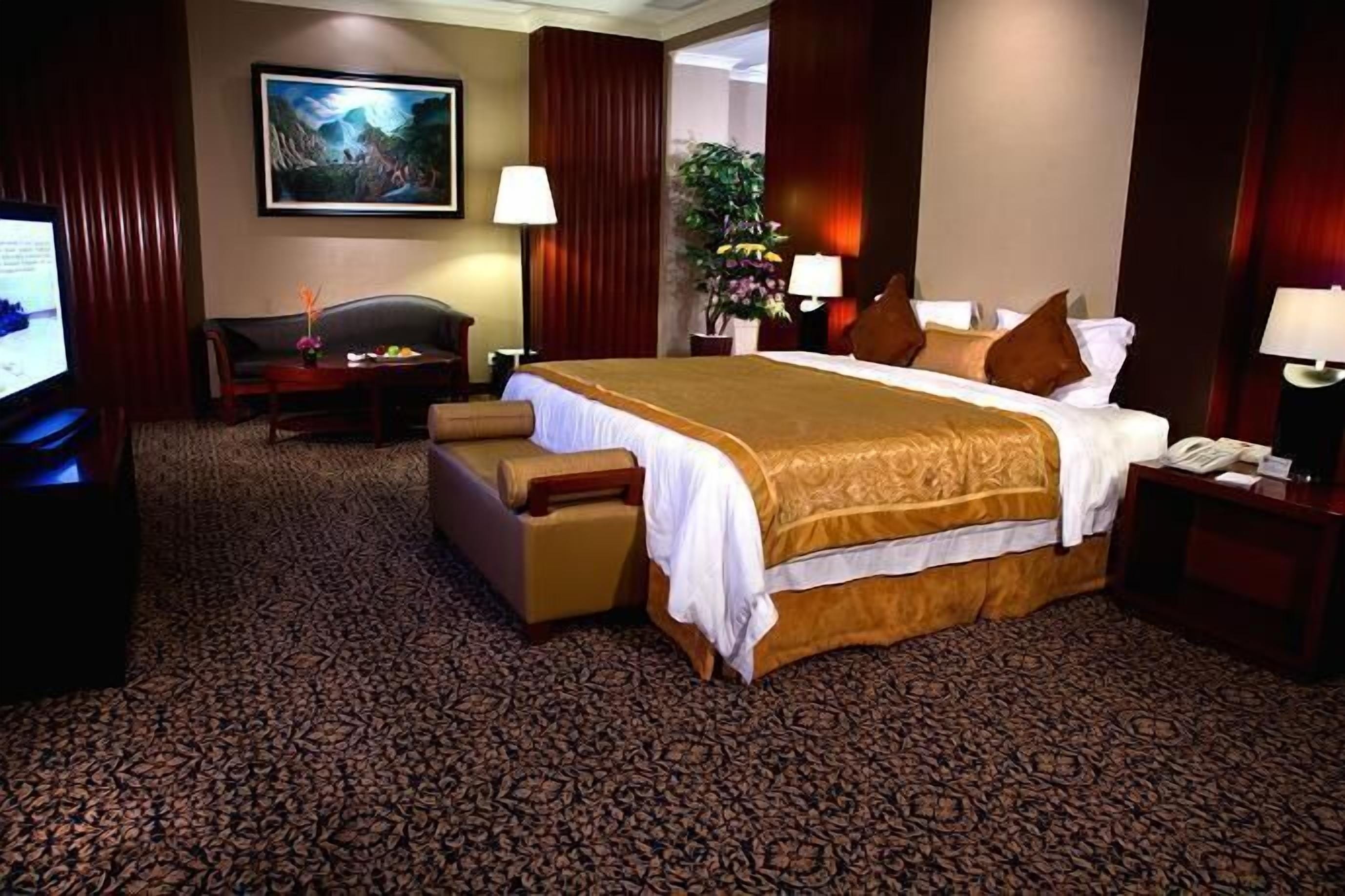 A hotel room with a large bed, a desk, a chair, a television, and a painting on the wall.