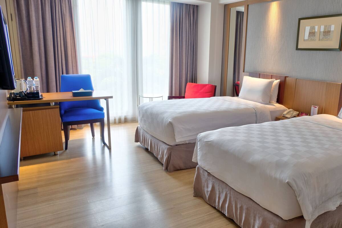 A hotel room with two beds, a desk with a chair, a coffee maker, and a telephone.