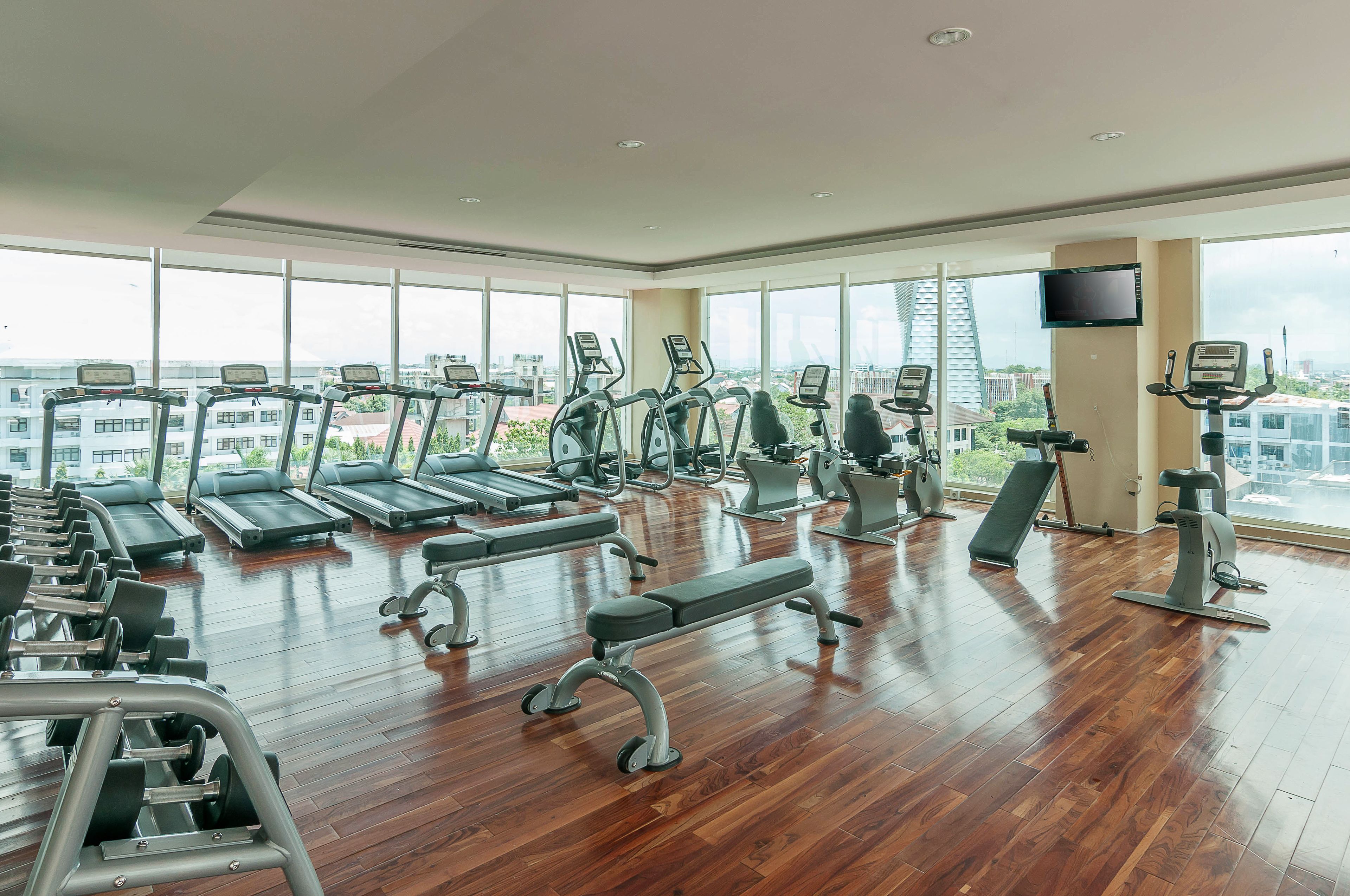 A spacious gym with treadmills, elliptical machines, and weight benches. Large windows offer views of the cityscape.