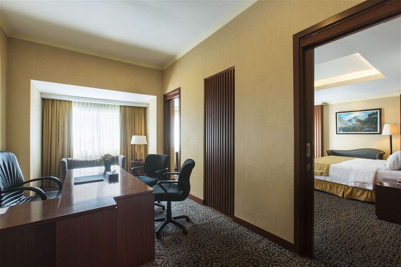 A hotel room with a large bed, a desk with two chairs, a window with curtains, and a painting on the wall.
