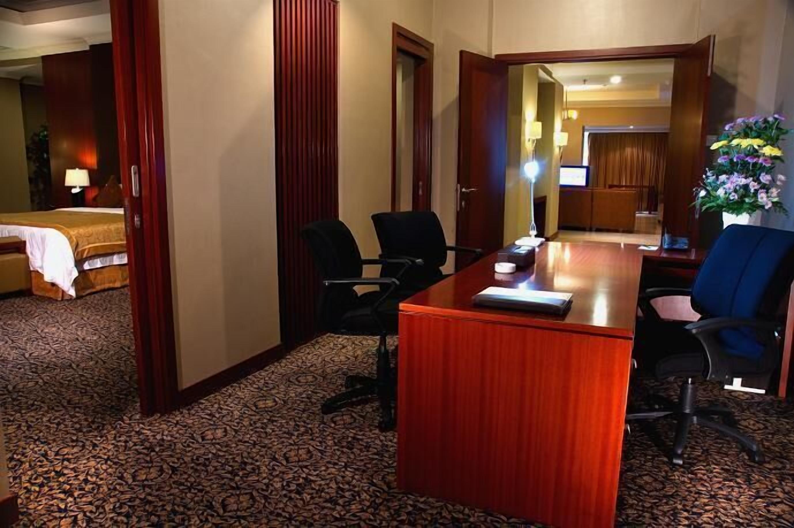A hotel room with a wooden desk, two chairs, a bed, and a carpeted floor.