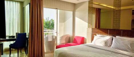 Habitación de hotel con cama, escritorio, silla y balcón con vista a palmeras.