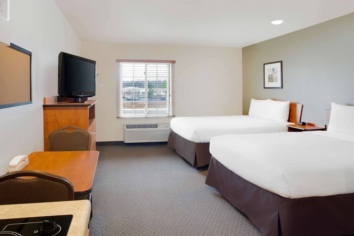 A hotel room with two beds, a desk with a telephone, a television on a stand, and a window with blinds.