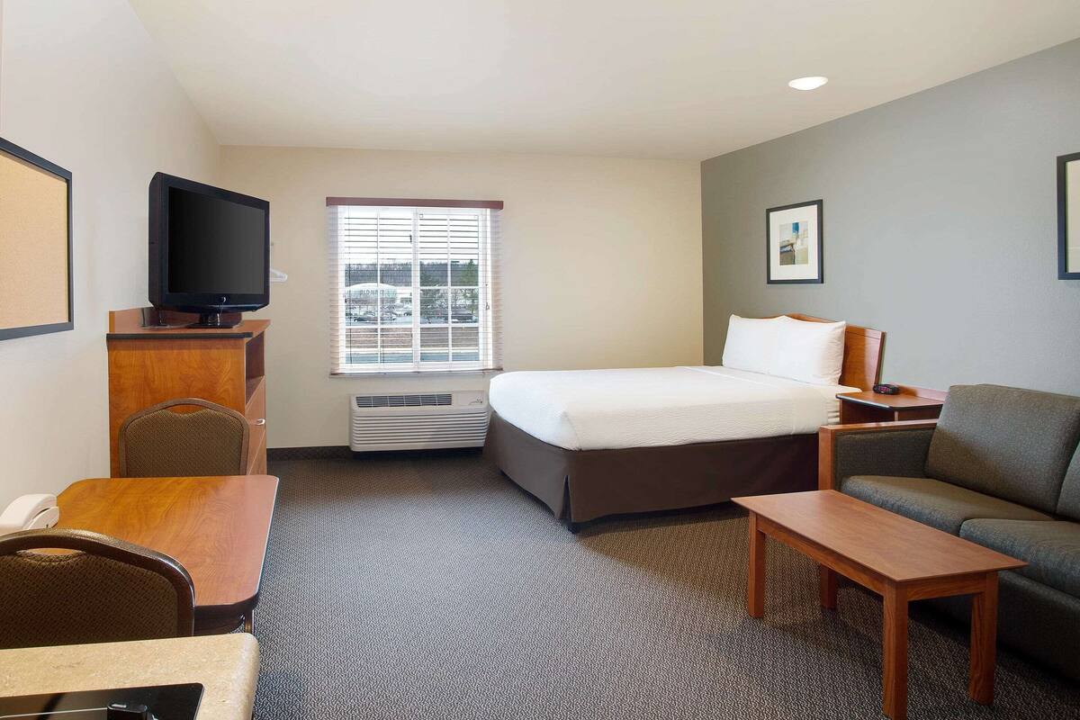 A hotel room with a bed, a sofa, a desk, a television, and a window with blinds.