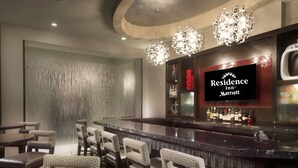 A bar area with a television displaying 'Residence Inn Marriott' branding, a bar counter with bottles, and a seating arrangement with chairs and tables. - Residence Inn Boston Needham (Needham)