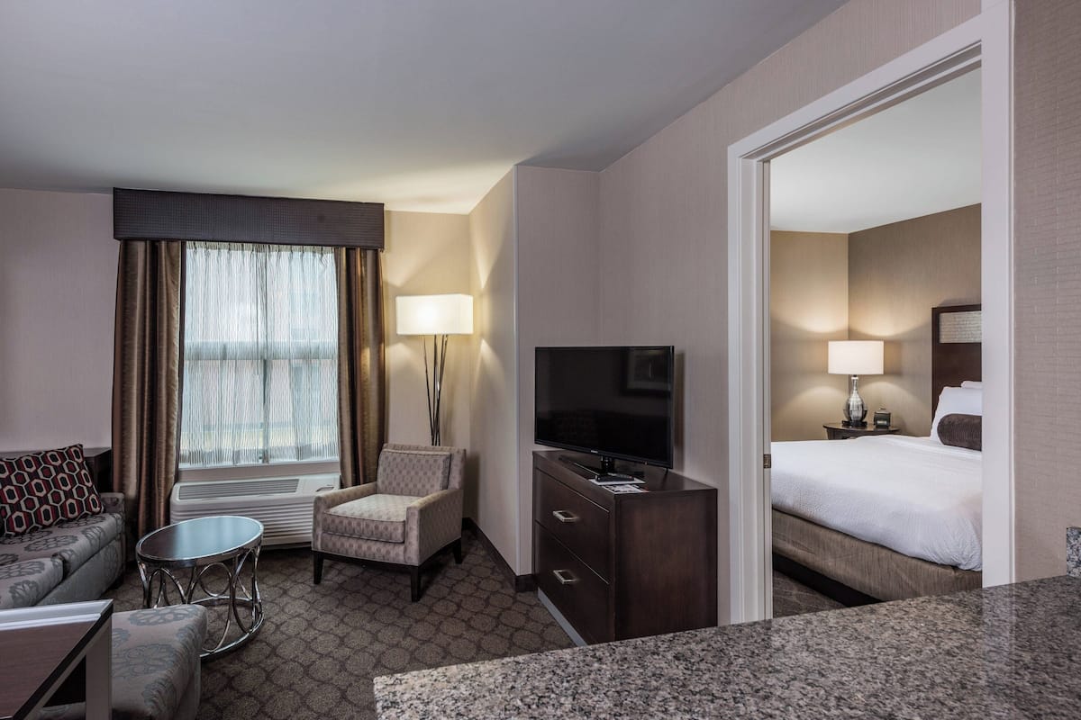 A hotel room with a bed, a TV, a desk, a chair, a lamp, and a window with curtains.