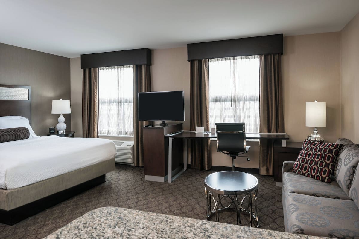 A hotel room with a bed, desk, chair, and a sofa.