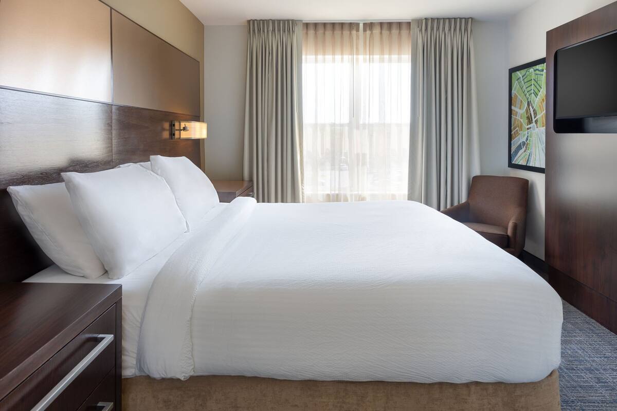 A hotel room with a large bed, a desk, a chair, a TV, and curtains.
