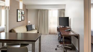 A hotel room with a bed, a desk with a computer, a chair, a sofa, and a TV.