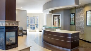 A modern reception area with a curved desk, a fireplace, and a view of the city through large windows. - Residence Inn Largo Medical Center Drive (Upper Marlboro)