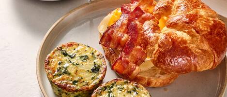 A plate with a croissant, two quiches, and a bowl of oatmeal.