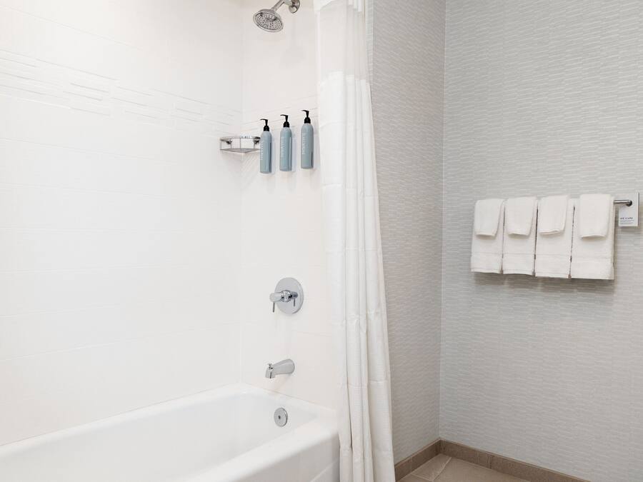 Ein Badezimmer mit einer Badewanne, einer Duschbrause und einem Handtuchhalter mit Handtüchern.