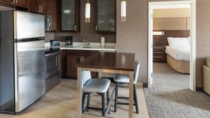 A modern kitchen with a stainless steel refrigerator, a built-in oven, and a coffee maker. There is a dining area with a wooden table and four chairs. The room has wooden cabinets and a large mirror above the sink. - Residence Inn Largo Medical Center Drive (Upper Marlboro)