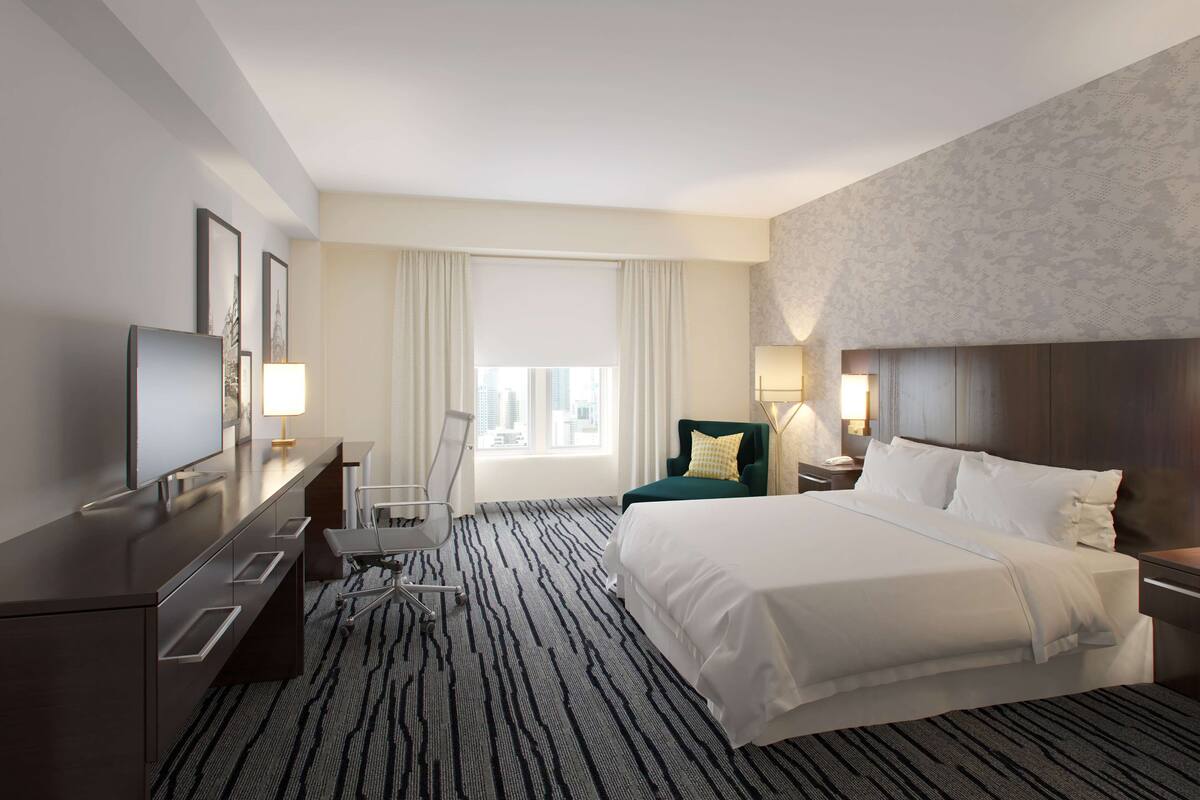 Una habitación de hotel con una cama grande, un escritorio con silla, televisión y ventana con cortinas.