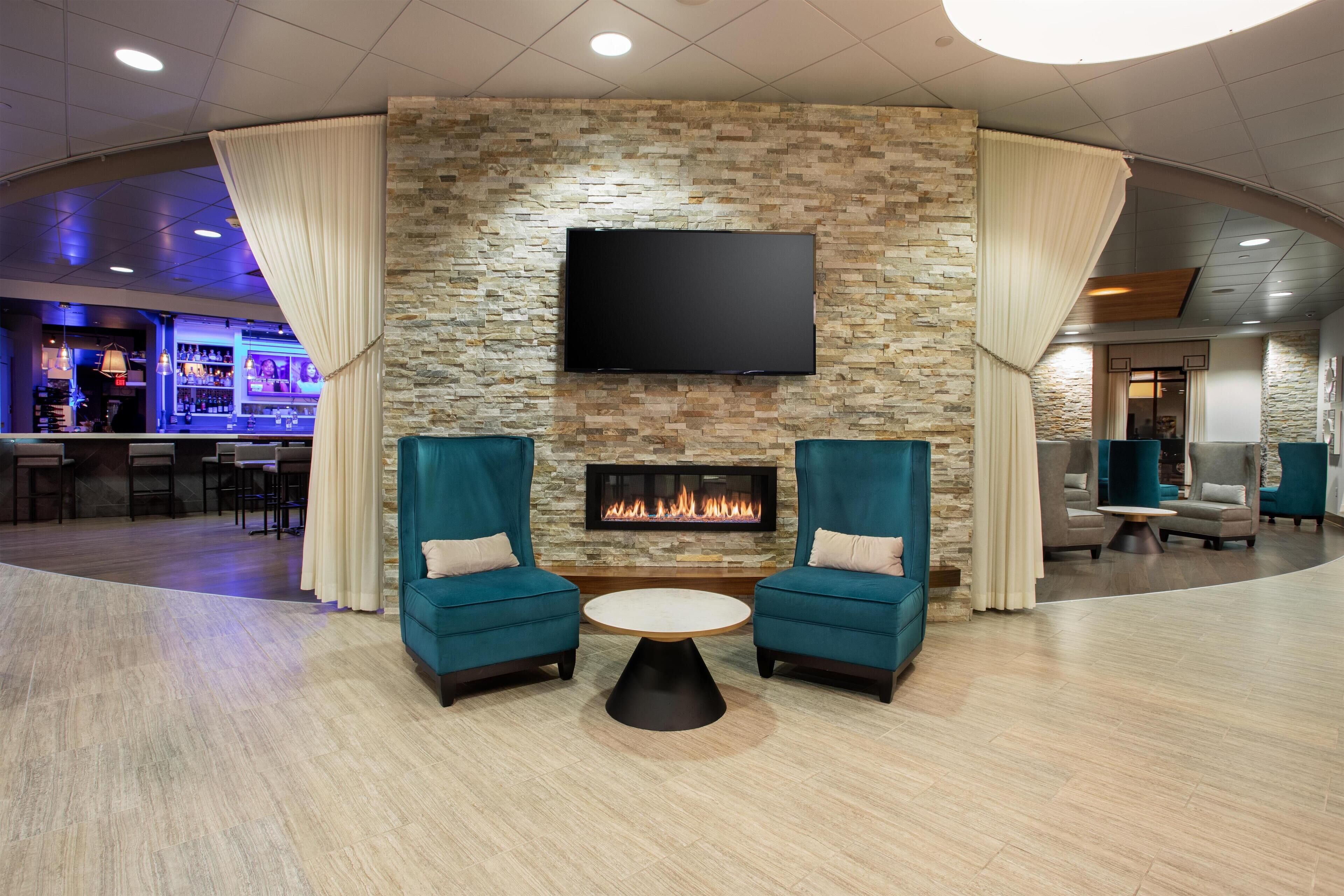 Un vestíbulo con pared de piedra, un televisor de pantalla plana, chimenea, sillones turquesa y una mesa de centro redonda.