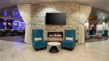 Un vestíbulo con pared de piedra, un televisor de pantalla plana, chimenea, sillones turquesa y una mesa de centro redonda.