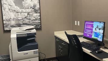 A hotel office with a desktop computer, a printer, and a large framed picture of a waterfall.