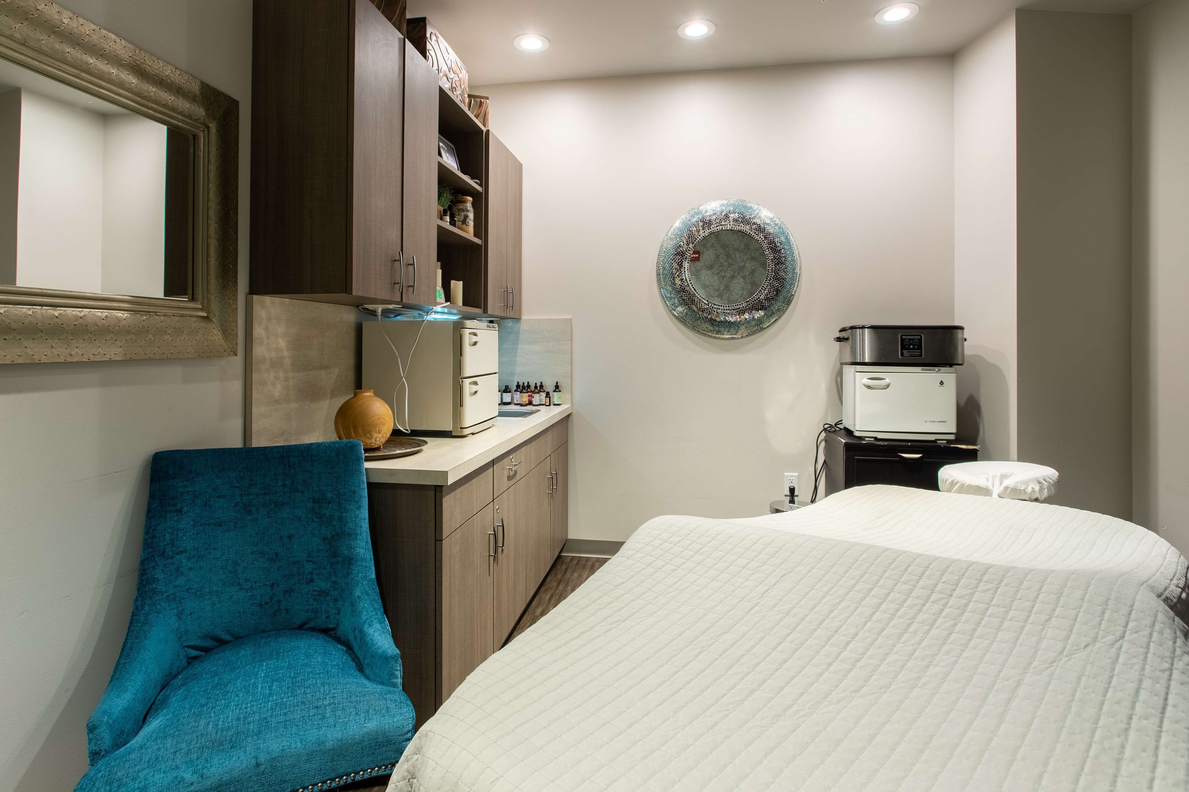 A hotel room with a bed, a blue armchair, a small table with a kettle, a microwave, and a wall-mounted plate.